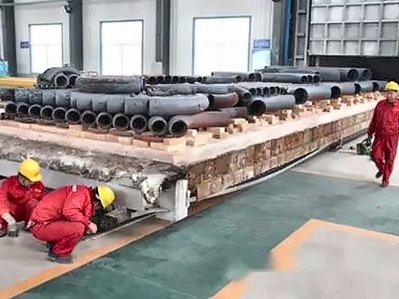 Heat-treatment loading — workers staging fittings on furnace cart